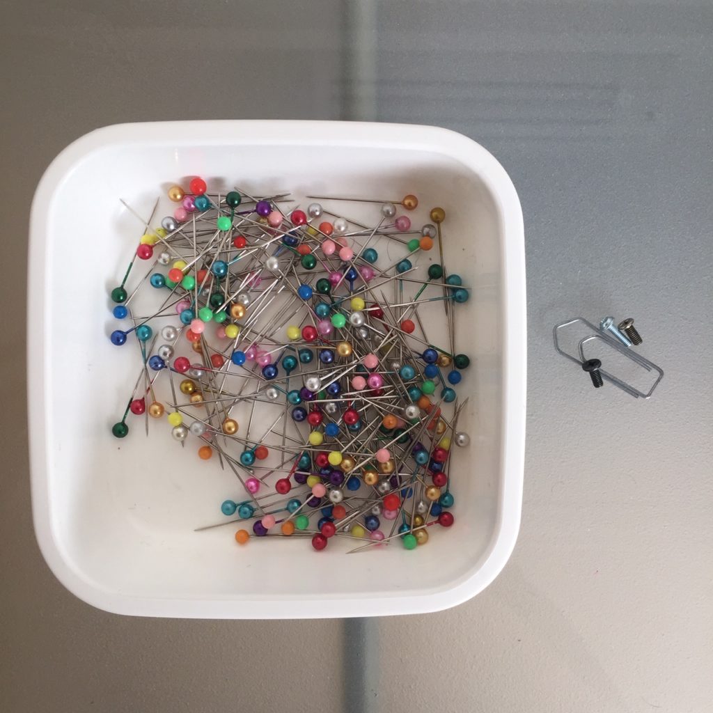Das Bild zeigt eine Dose mit Stecknadeln, kleine Schrauben und eine Büroklammer | Kristina Kral, Minimalismus